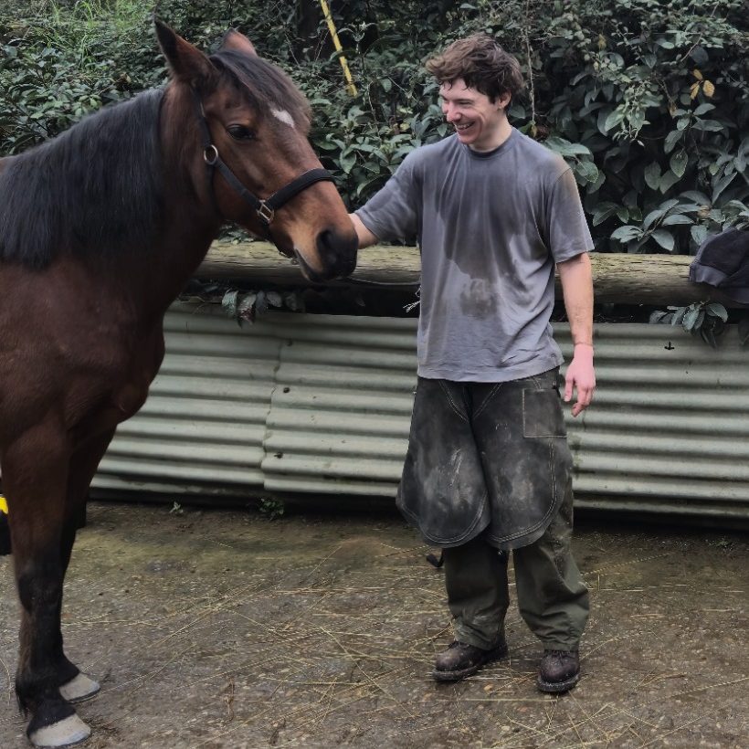 Un hombre sonriente acaricia a un caballo en un entorno natural y húmedo.