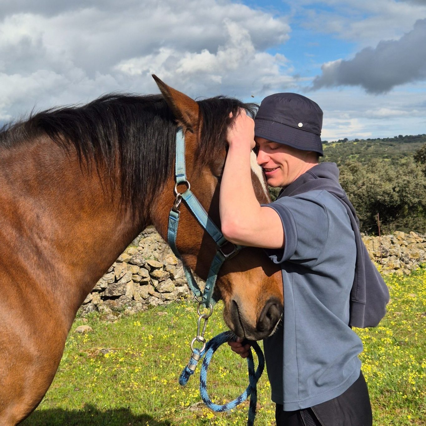 Persona abrazando un caballo en un paisaje campestre con cielo nublado.